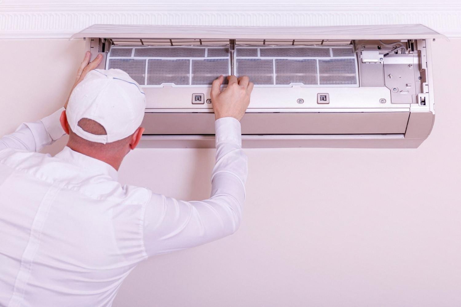 Technician in white uniform servicing a wall-mounted split air conditioner in a UAE apartment