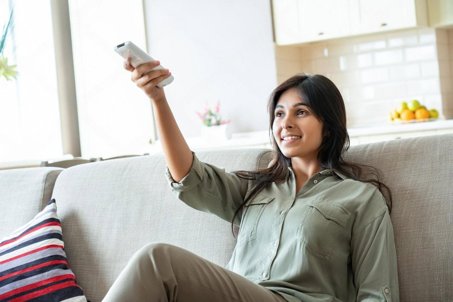Woman relaxing on a sofa using an air conditioner remote in a cool UAE home