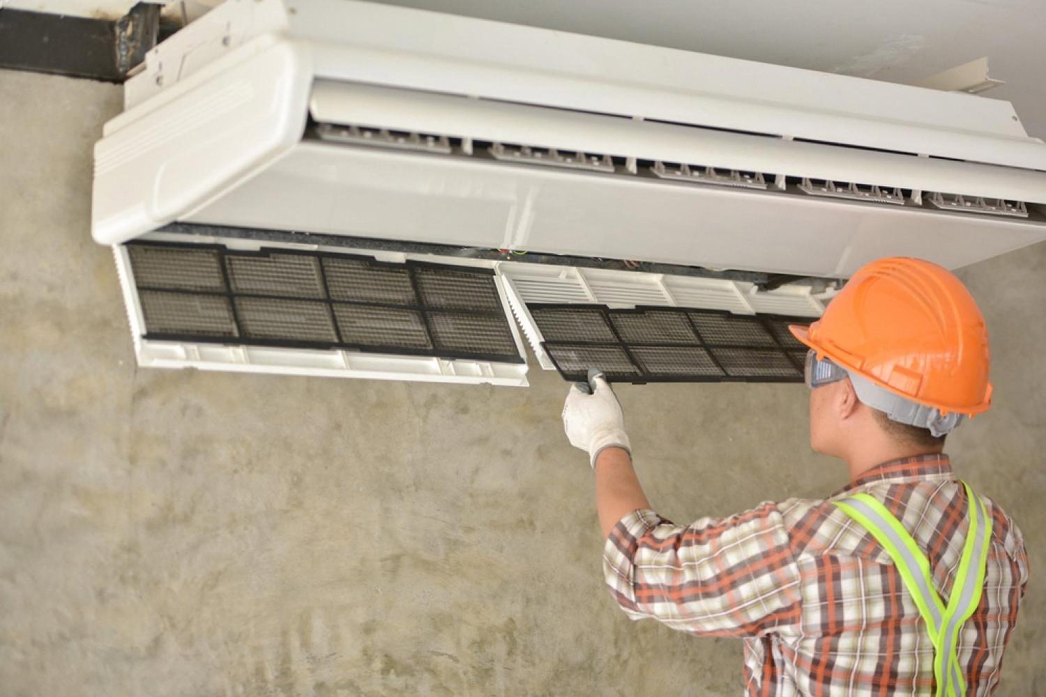 Certified installer in hard hat and safety vest fitting a ceiling cooling unit at a Dubai property